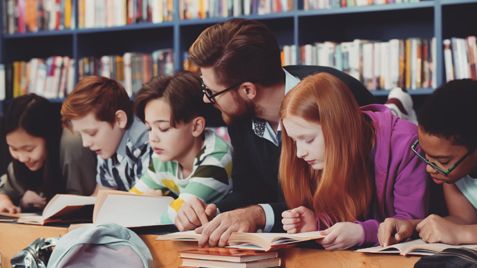 Teacher and kids lying on floor reading book in library. Portrait of multiracial schoolchildren and teacher reading textbook on floor having lesson in school library