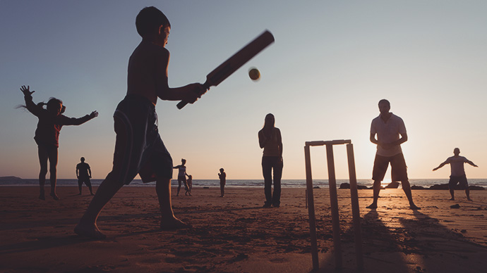 Family playing cricket on beach at sunset