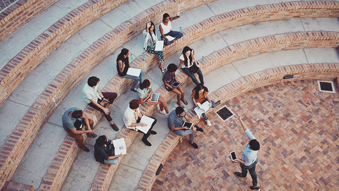 Students having class with book and tablets, in outside auditorium. Students with raised hands