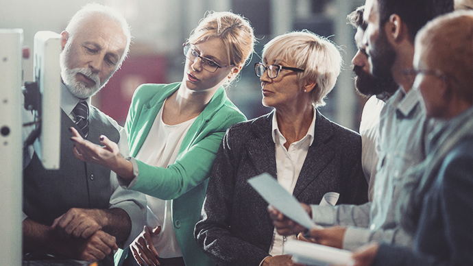 Closeup of senior manager and a mid 30's coworkers looking at certain printed data and standing in front of a CNC cutting machine at a wood production facility.